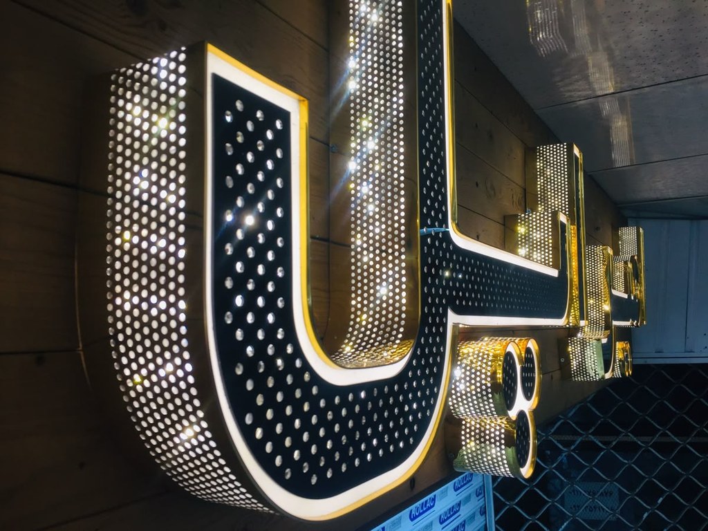 Lettres boîtiers rétroéclairées noir et or, tôle perforée, montées sur une façade en bois